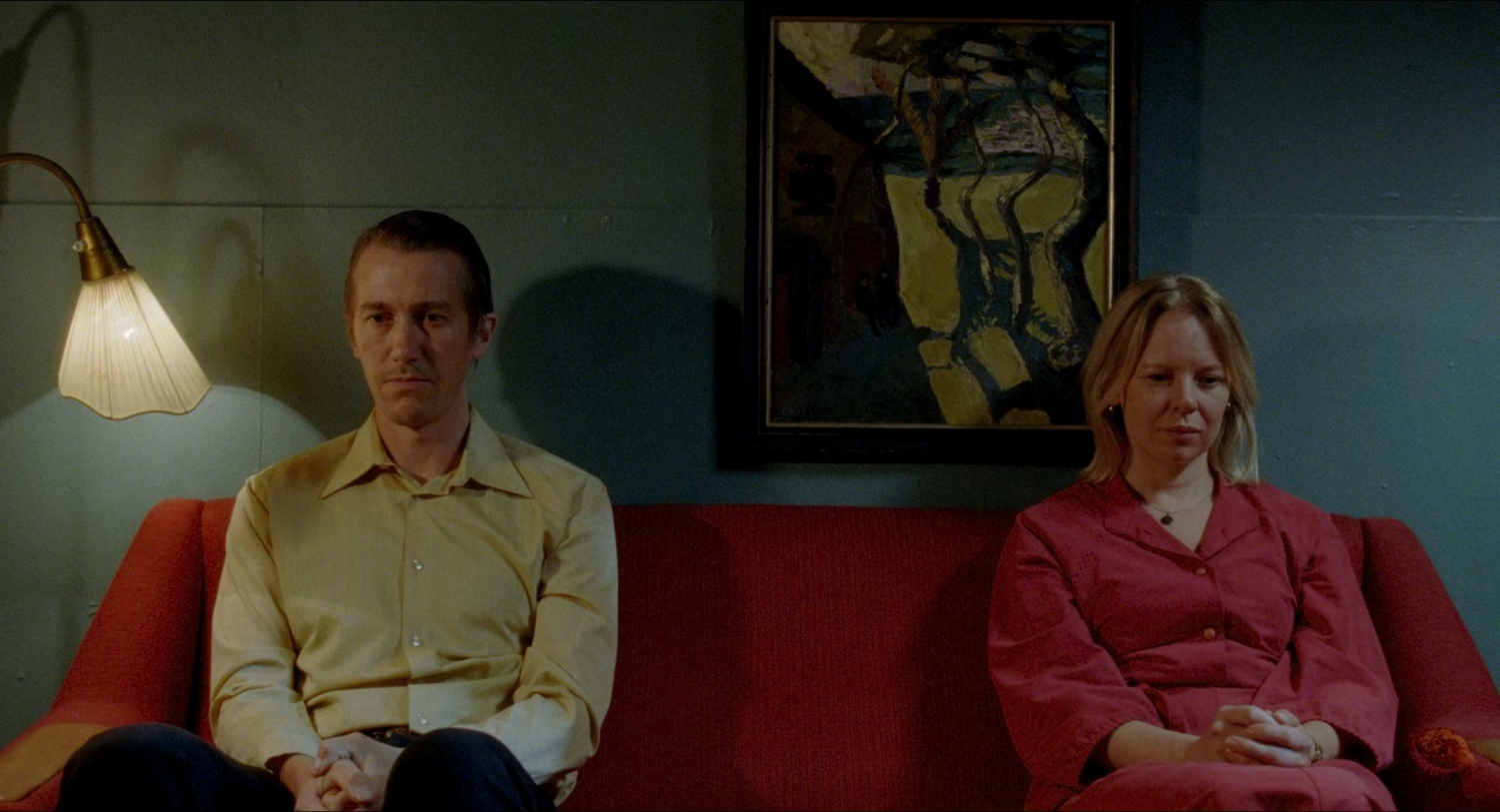 A man and a woman sitting on a red couch in a room with green walls