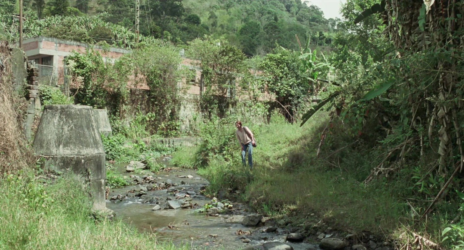 A woman in the distance next to a river with lush vegetation around it
