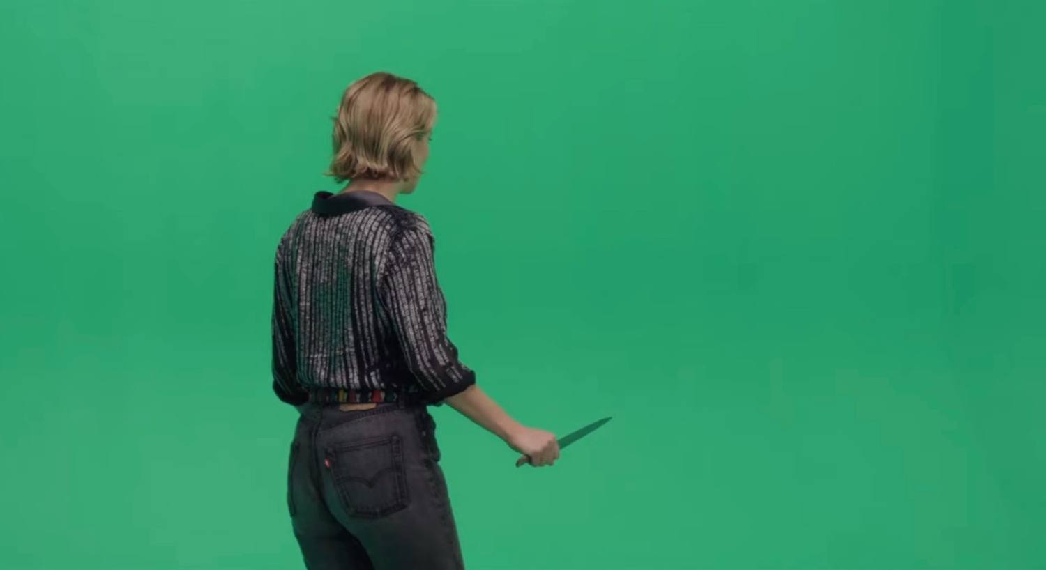 Woman holding a knife facing away in front of a green screen