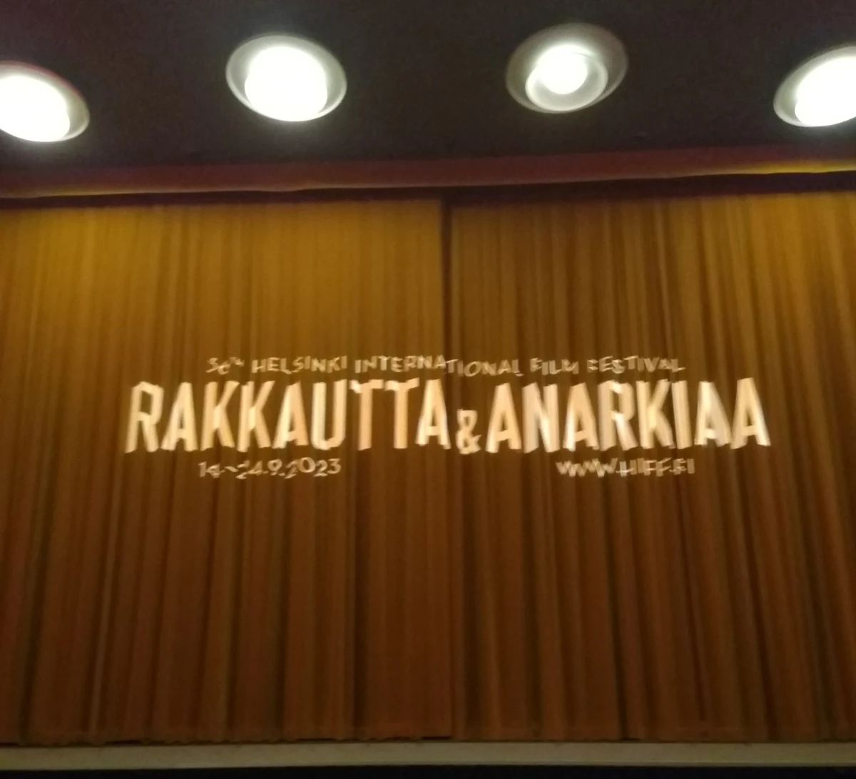 Blurry picture of beige curtains with the logo of Helsinki International Film Festival projected on them.